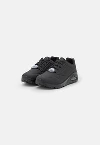 Chaussures de sport noires avec une tige texturée et une semelle en caoutchouc. Comprend de lacets épais et un coussin d'air visible dans le talon.