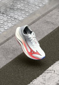 Scarpa da corsa con una tomaia grigia e bianca, dettagli rosa e un design elegante. Presenta una suola testurizzata e un sistema di allacciatura per una vestibilità sicura.