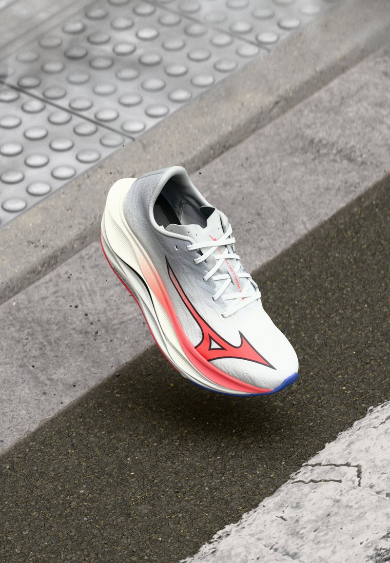 Scarpa da corsa con una tomaia grigia e bianca, dettagli rosa e un design elegante. Presenta una suola testurizzata e un sistema di allacciatura per una vestibilità sicura.