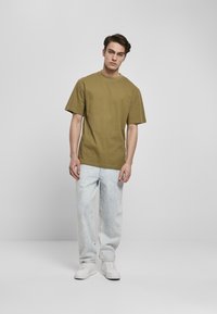 Tricou verde oliv cu guler rotund și mâneci scurte, asortat cu blugi decolorati, lejeri, de culoare albastru deschis și adidași albi.