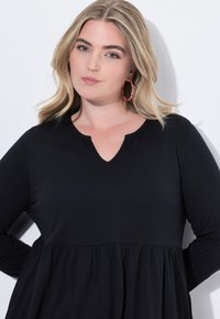 Haut noir à manches longues avec un col en V et un design évasé, fabriqué à partir d'un matériau doux avec une texture lisse.