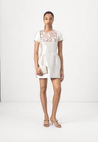 Lyhyt mekko vaaleanharmaasta teksturoidusta kankaasta, jossa on pitsinen bodice-osa. Mukana kirjailtu vaalean värinen clutch ja hihnalliset kengät.