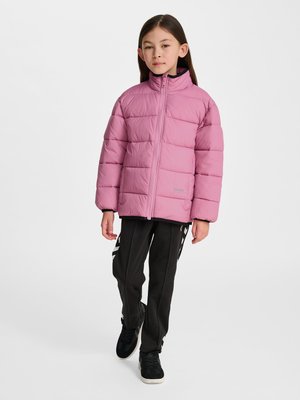 Ung pige går fremad iført en pink dunjakke, sorte træningsbukser med hvide striber og sorte sneakers mod en hvid baggrund.