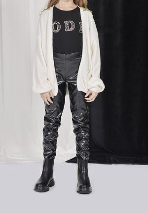 Witte gebreide cardigan met gekleurde kralen, zwart graphic t-shirt, glanzende zwarte leren broek en zwarte enkellaarzen.