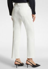 Pantaloni in denim bianco a gamba larga con vita media, dotati di tasche posteriori e una superficie liscia, abbinati a décolleté neri a punta.