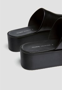 Sandales à plateforme noires avec une tige en cuir lisse, un design à bout ouvert et une semelle épaisse texturée. Marque visible sur la semelle intérieure.