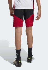 Black and red sports shorts with a mesh texture, side stripes, and a contrasting design. Worn with black socks and soccer cleats.