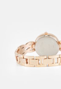 Orologio in oro rosa con bracciale a maglie. Presenta una cassa rotonda e una finitura metallica liscia. Sul retro sono incisi i dettagli del marchio.