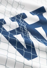 Hvidt stof med et stort blåt motiv bestående af geometriske former, overlejret med et lyseblåt gittermønster.