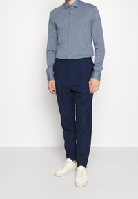 Lichtblauwe overhemden met lange mouwen en een kraag, met subtiele branding, gecombineerd met hoge marineblauwe broeken en witte sneakers.