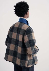 Kontrollitud vilditud villane jakk tumesinisel ja beežil, millel on mugav lõige, ümarad õlad ja sinine krae. Tekstureeritud kangas nähtavate õmblustega.