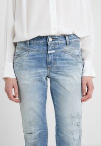 Jeans de mezclilla azul desvanecidos y desgastados con cintura de altura media y cinco bolsillos, con un ligero deshilachado y un cierre de botón en la parte delantera.