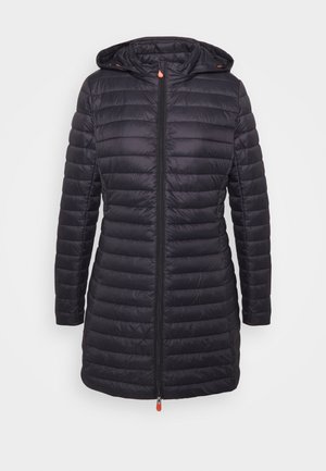 Veste matelassée noire rembourrée jusqu'aux genoux avec capuche, fermeture éclair avant avec tirettes orange, et manches longues sur fond blanc uni.