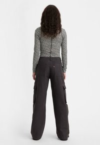 Zwarte cargobroek met zijzakken en een hoge taille, gecombineerd met een aansluitend langemouwtop met een klein bloemenpatroon.