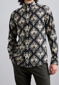 Camicia nera con bottoni, decorata con un elegante motivo floreale crema, maniche lunghe e colletto. Il tessuto appare liscio con una finitura robusta.