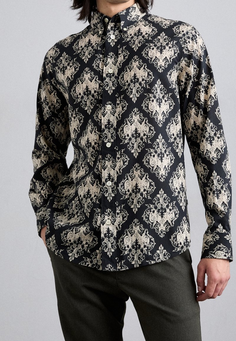 Camicia nera con bottoni, decorata con un elegante motivo floreale crema, maniche lunghe e colletto. Il tessuto appare liscio con una finitura robusta.