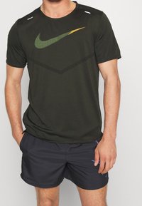 La camiseta deportiva negra presenta un logo de Nike en verde y amarillo, tejido texturizado y mangas cortas, combinada con pantalones cortos oscuros.