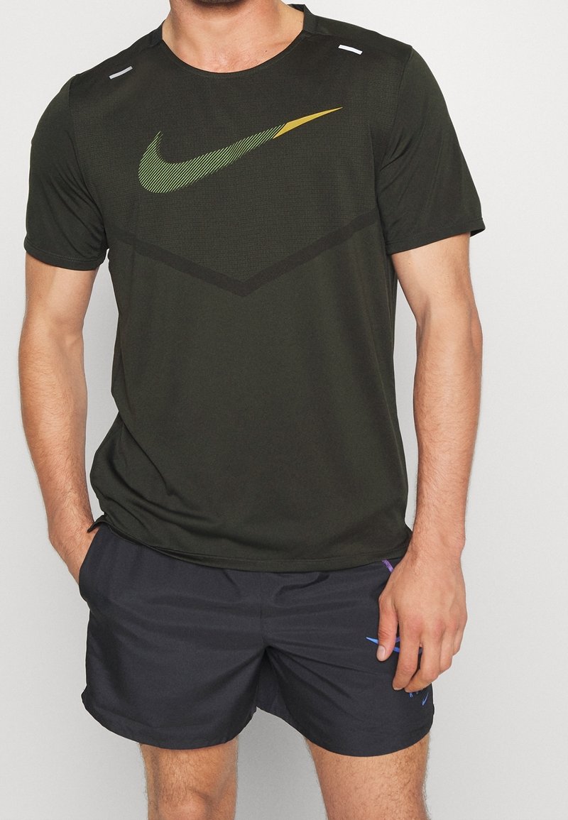 La camiseta deportiva negra presenta un logo de Nike en verde y amarillo, tejido texturizado y mangas cortas, combinada con pantalones cortos oscuros.