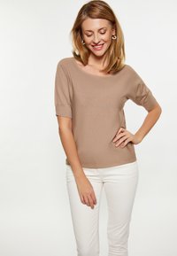 Beige, lyhythihainen paita, jossa on leveä pääntie ja ribbitekstuuri, yhdistetty valkoisiin slim-fit-housuihin. Yksinkertainen muotoilu, kevyt kangas.