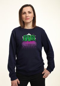 Felpa blu navy con design di un personaggio verde pixelato su uno sfondo a griglia viola. Il materiale sembra morbido, con maniche lunghe e vestibilità rilassata.