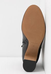 Chaussure habillée en cuir noir montrant une semelle lisse couleur tan avec les inscriptions « Made in Italy » et la taille 37, positionnée debout sur un fond blanc.