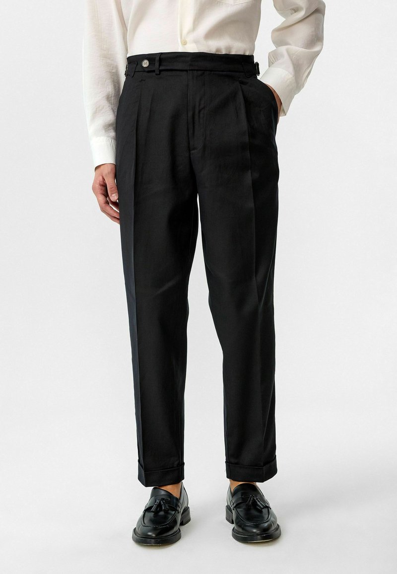 Zwarte op maat gemaakte broek met een hoge taille, plooien, zijzakken en contrasterende knopen. Gemaakt van lichtgewicht stof met een gladde textuur.