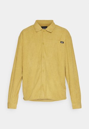 Camicia a maniche lunghe in velluto a coste color giallo senape con colletto, chiusura con bottoni sulla parte anteriore, tasca sul petto e piccola etichetta del marchio nera sulla tasca.