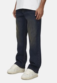 Granatowe dżinsy z prostym krojem i delikatnym wyblaknięciem. Noszone z białymi trampkami z wieloma paskami i teksturowanym wzorem.