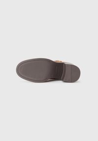 Suela de zapato de goma marrón con ranuras horizontales para tracción, bordes redondeados y un leve tacón. Diseño limpio y minimalista.
