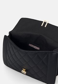 Czarna pikowana torebka z gładką fakturą, z złotym zapięciem i metką marki "ANNA FIELD" wewnątrz. Wnętrze torebki wykonane jest z jednolitego materiału.