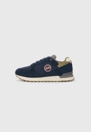 Navy blue sneakers with suede and textile upper, featuring a round red logo on the side, beige sole, and gray detailing on the tongue.