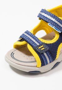 Modré a žluté voděodolné sandály s textilním svrškem a suchými zipy, měkkou gumovou podrážkou a perforovanou stélkou.