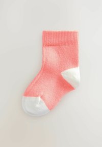 Coral pink sock with a ribbed texture and white toe and heel accents. Mid-calf length with a seamless design. Soft knit material.