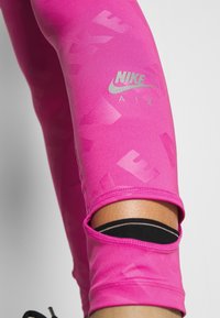 Leggings rosa con un motivo sottile e un logo Nike al ginocchio. Presentano aperture nella parte bassa della gamba, una texture liscia e materiale elasticizzato.