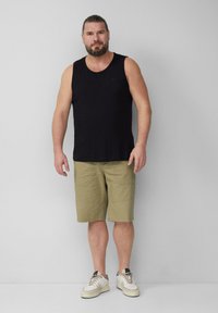 Schwarzes ärmelloses Tanktop, khakifarbene Shorts und weiße Sneakers. Lässiger Look mit lockerer Passform und strukturiertem Stoff.