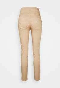 Jeans skinny beige con una texture liscia, vita media, tasche posteriori e dettagli di cucitura minimi. Stilizzati per una silhouette aderente.