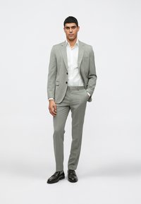 Traje gris claro con un patrón texturizado, diseño ajustado, cierre de dos botones y botones negros. Combinado con una camisa blanca de vestir y zapatos negros.