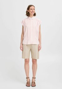 Camisa de cuadros rosa y blanca con cuello y mangas cortas, combinada con pantalones cortos beige hasta la rodilla y sandalias de tacón marrones.