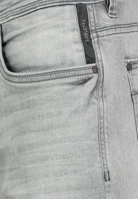 Gray denim jeans feature a subtle washed texture, front pockets, and a label reading "SUBLEVEL" on the waistband.