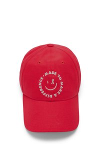 Red baseball cap made of cotton, featuring a white embroidered smiley face and text "MADE TO MAKE A DIFFERENCE" around it.