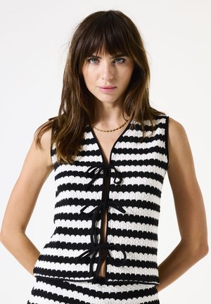 Top sans manches rayé noir et blanc en maille texturée, avec un décolleté en V et des accents noués sur le devant.