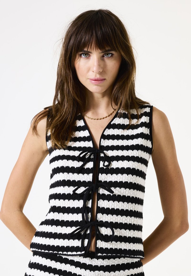 Top sin mangas a rayas blancas y negras con un material de punto texturizado, que presenta un escote en V y detalles de lazo en la parte delantera.