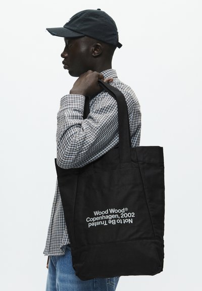 Fekete vászontáska, téglalap alakú, strapabíró pántokkal, fehér szöveggel: "Wood Wood Copenhagen, 2002".