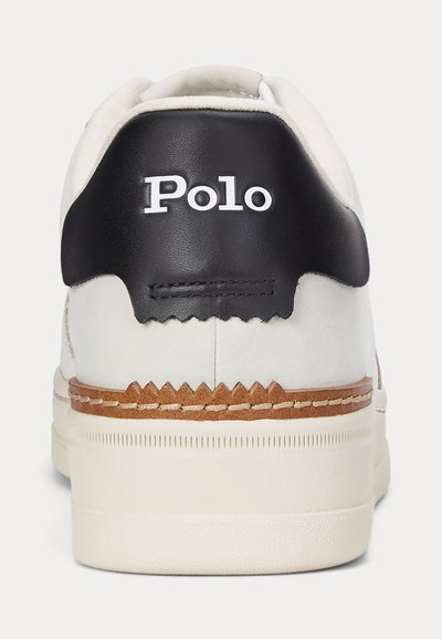 Bijeli peta tenisice s bež potplatom, smeđim šavovima i crnim kožnim zakrpom na kojem je bijeli tekst "Polo".