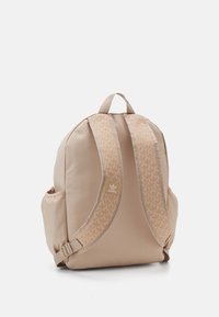 Béžový látkový batoh s polstrovanými popruhy zdobenými listovým vzorem, s horním úchopem, boční kapsou a malou štítkovou logou vpředu.