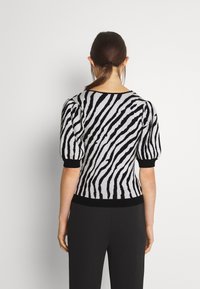 Jersey de punto a rayas blancas y negras con mangas cortas abullonadas, escote redondeado y dobladillo inferior negro ajustado.