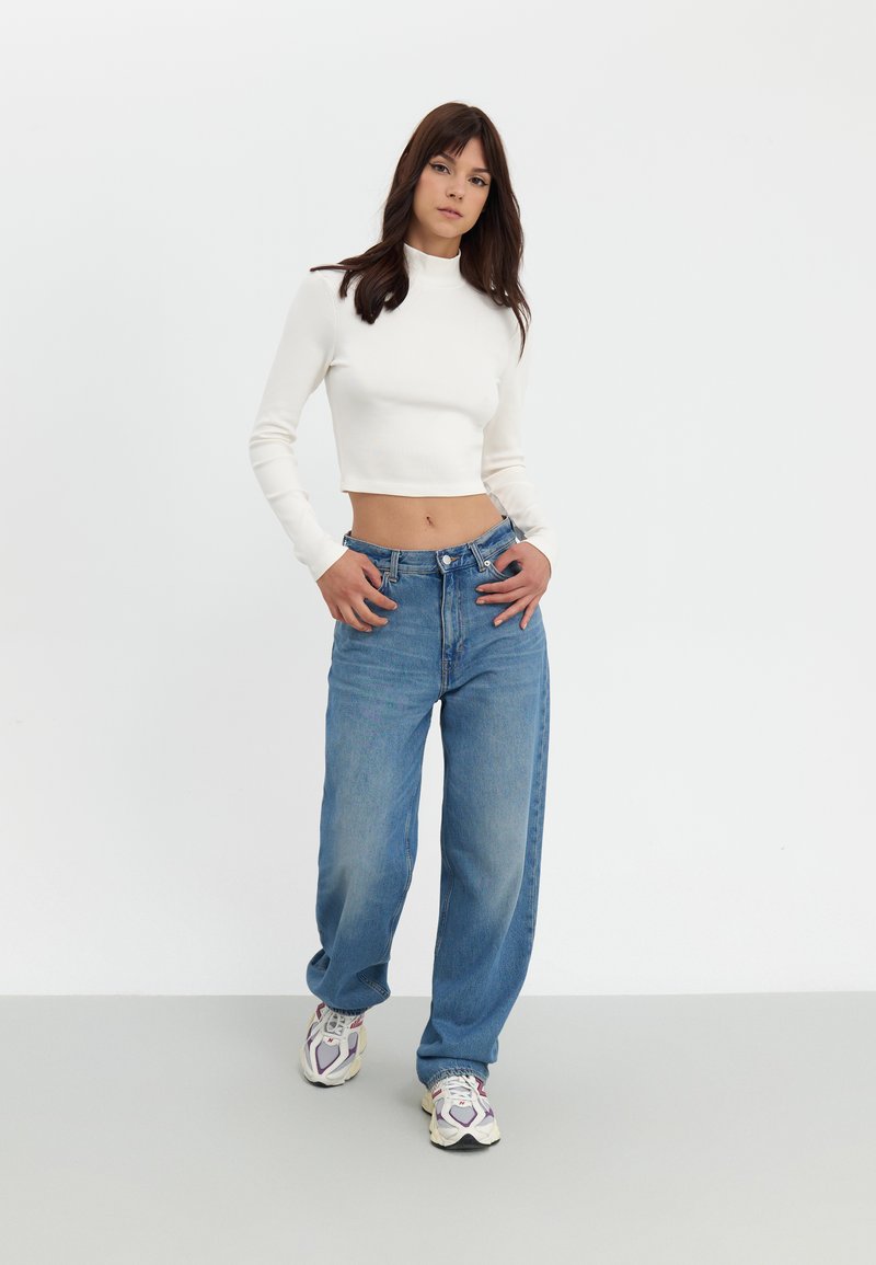 White ribbed crop top paired with light blue wide-leg jeans and multicolored athletic shoes, set against a neutral background.