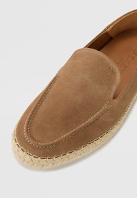 Bruna mockaskor i slip-on modell med rund tå, sömdetaljer och en flätad jutesula. Slät textur med minimala accenter.