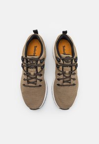 Baskets marron clair avec tige en textile, lacets noirs et semelle en caoutchouc. Logo sur la semelle intérieure et languette au talon.