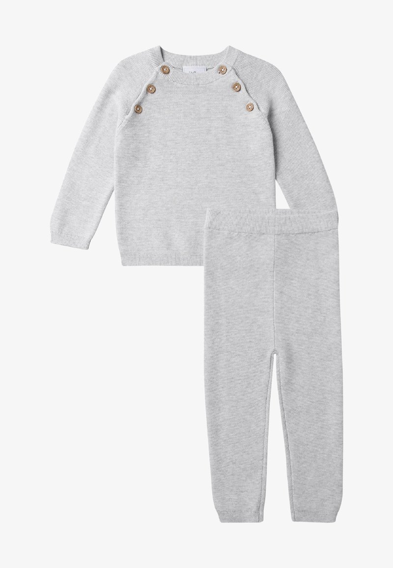 Grijze gebreide trui met zes bruine knopen op de schouder, gecombineerd met bijpassende broek met elastische tailleband. Beide stukken hebben een ribbelstructuur.